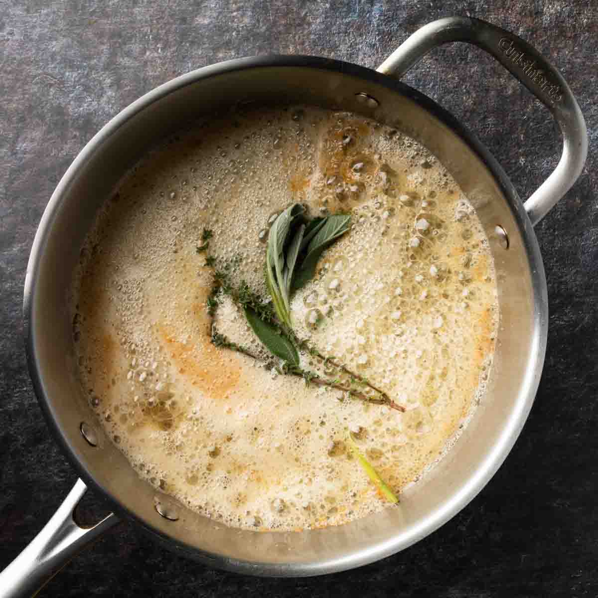 Foamy butter in a pan with a spring of fresh thyme and sage leaves. 