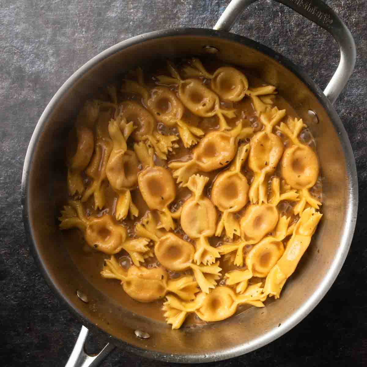 Homemade caramelle pasta simmering in a pan of brown butter balsamic sauce.