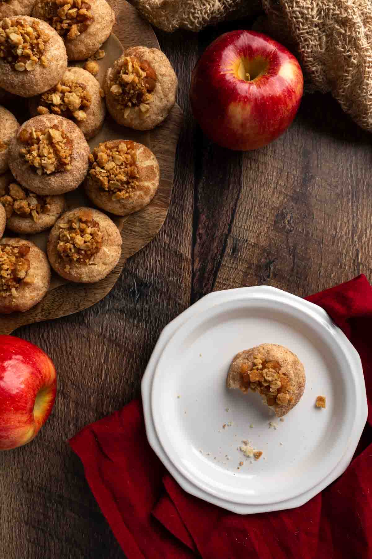 A plate with a bitten cookie next to a big platter of apple crumble cookies. 