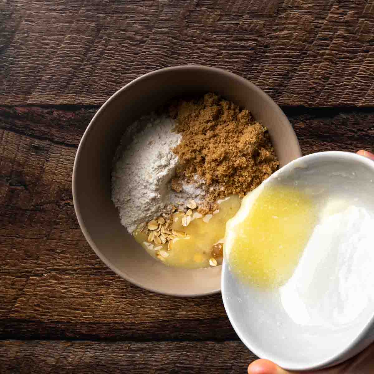 Pouring melted butter into a bowl of oat crumble toppings. 