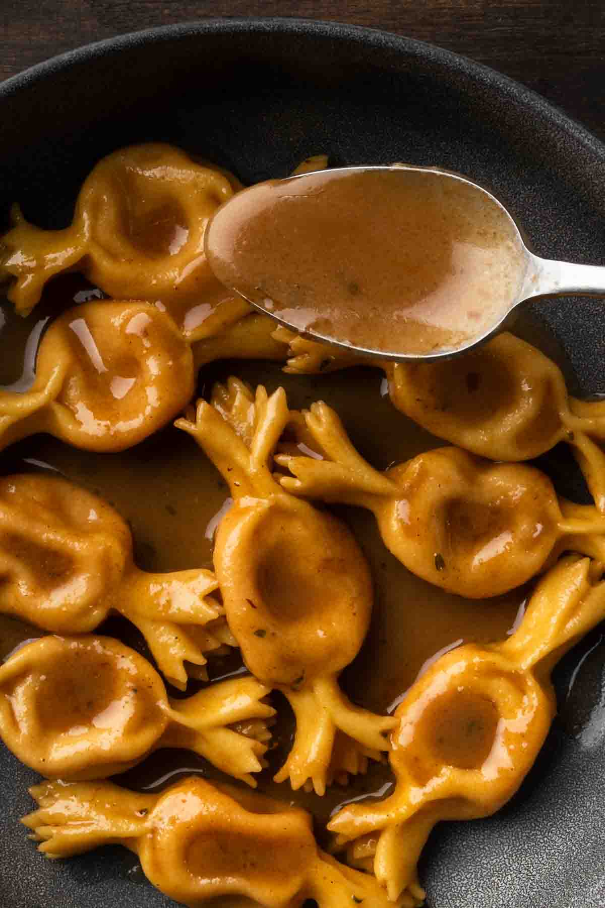 A spoon labeling brown butter balsamic sauce over a plate of pasta.