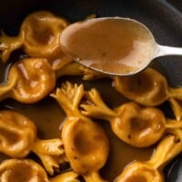 A spoonful of brown butter balsamic sauce over a big bowl of stuffed pasta.