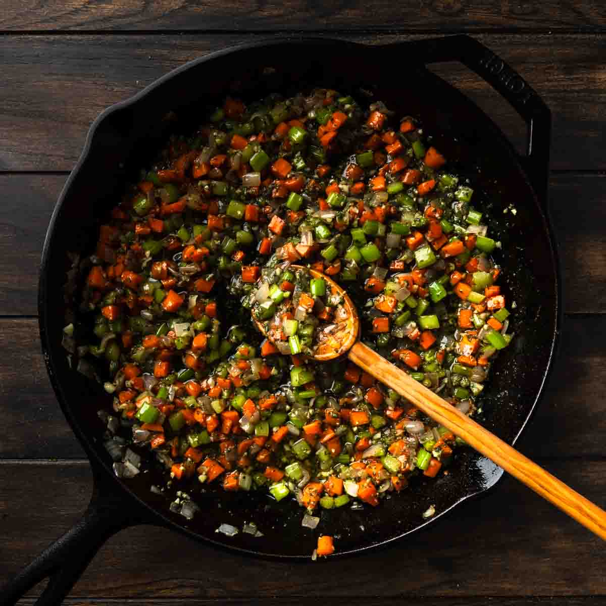 A skillet full of cooked mirepoix seasoned with minced garlic and lots of herbs.