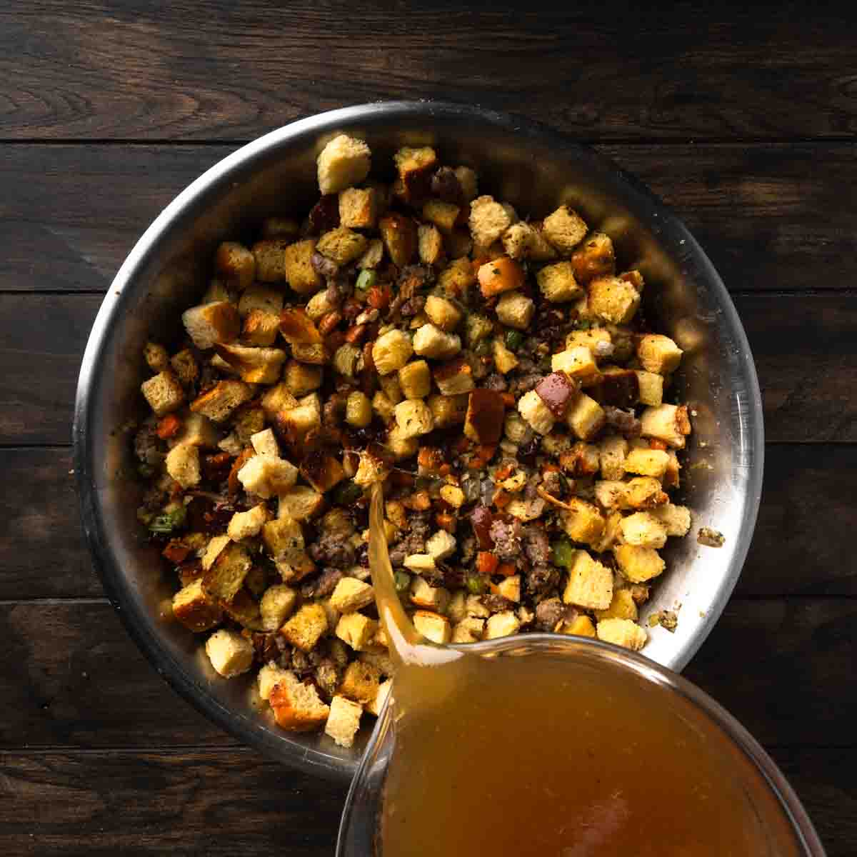 Adding turkey stock to a big bowl of stuffing.