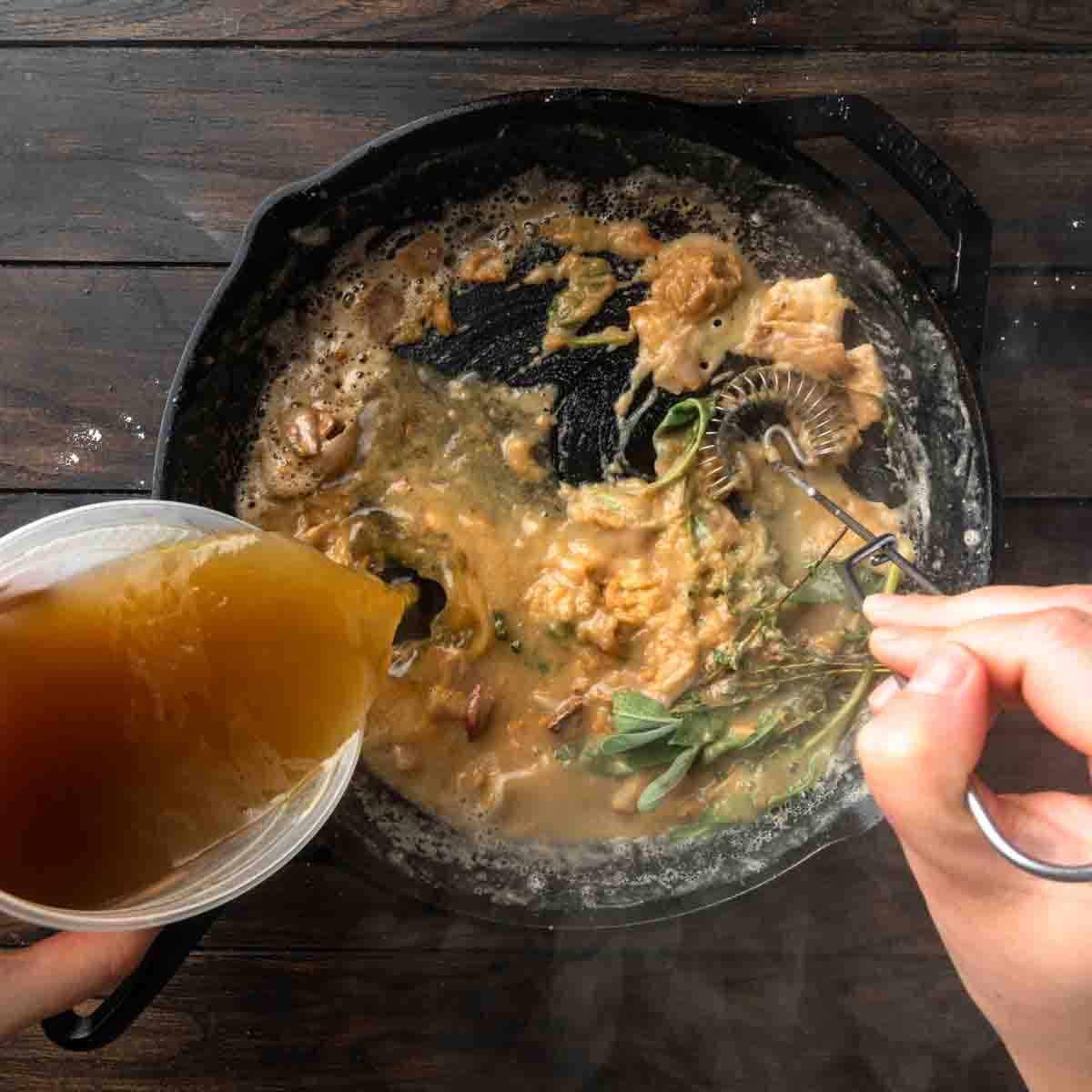 Slowly whisking a steam of turkey stock into the skillet of roux.