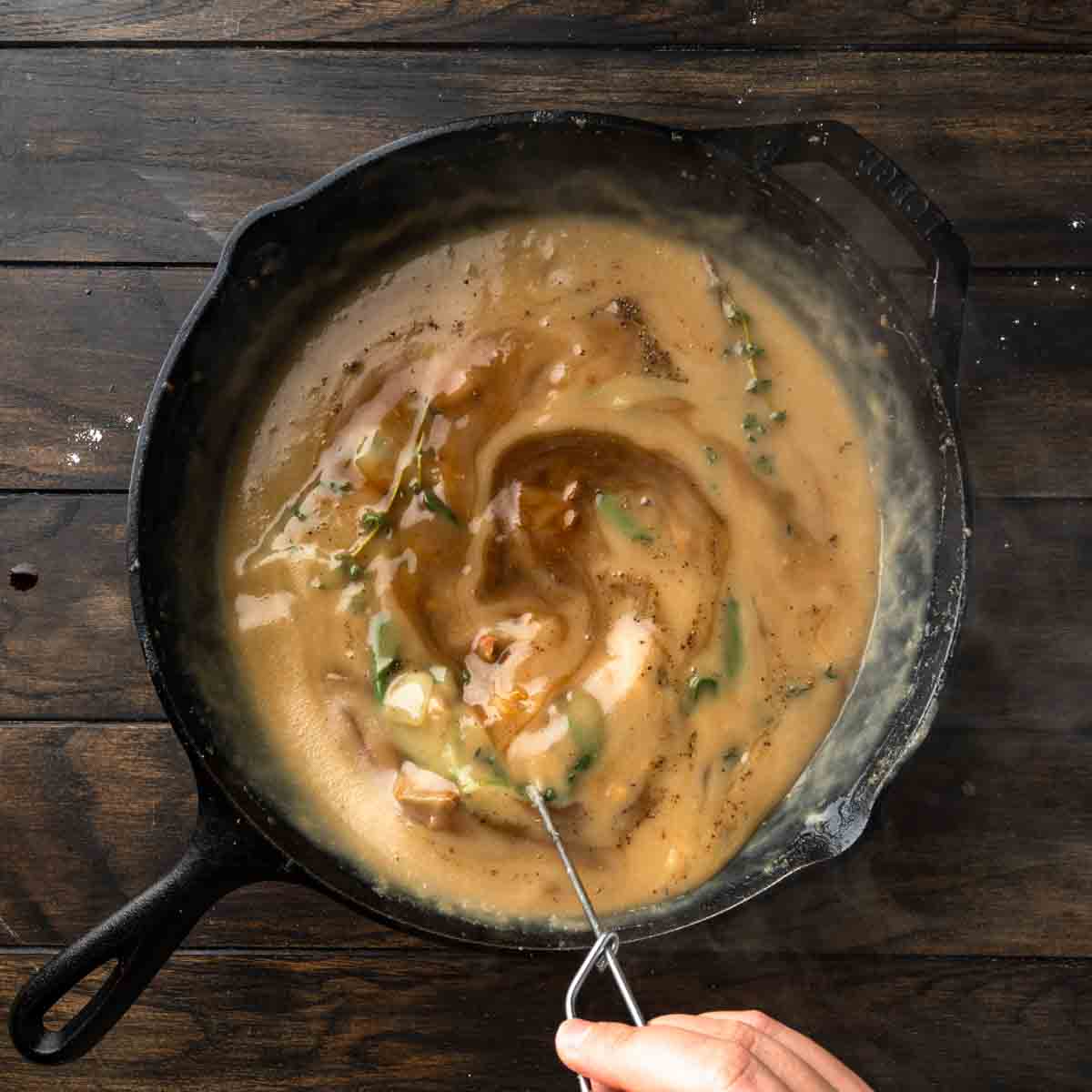 Simmering turkey gravy in a skillet with shallots, garlic and herbs.
