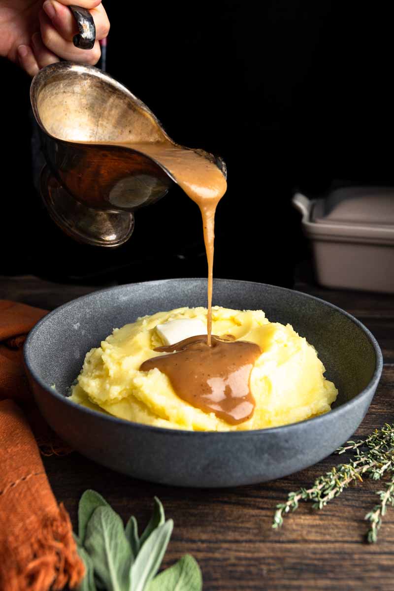 Pouring a boat of turkey gravy over a bowl of mashed potatoes.