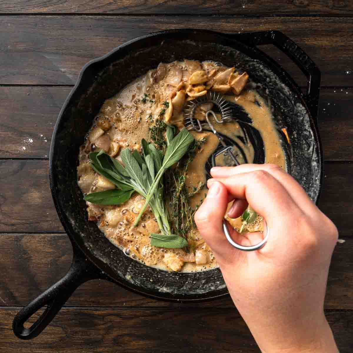 Fresh sage and thyme a top a skillet full of gravy roux. 