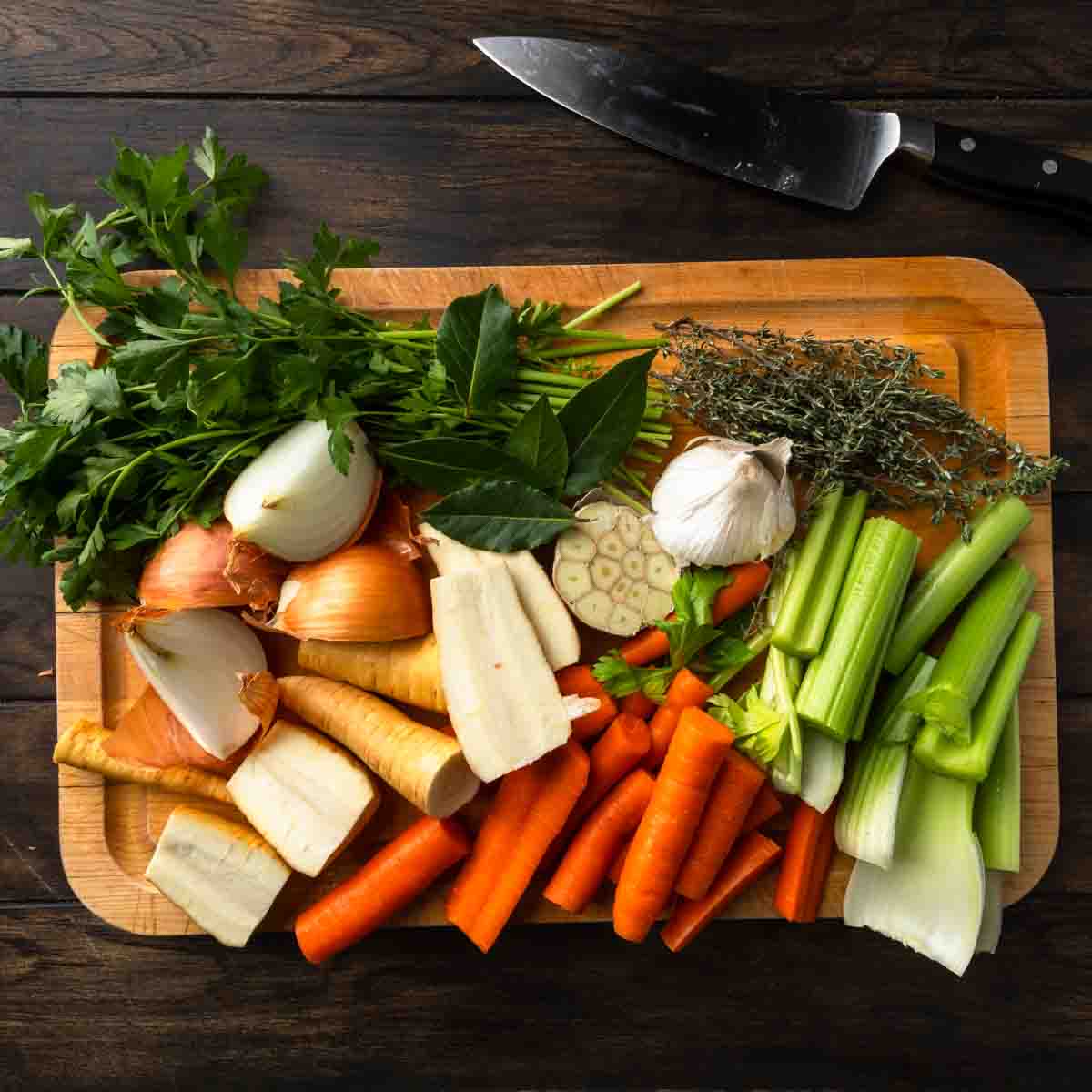 Onions, carrots, parsnips, celery and fresh herbs prepped on a cutting board.