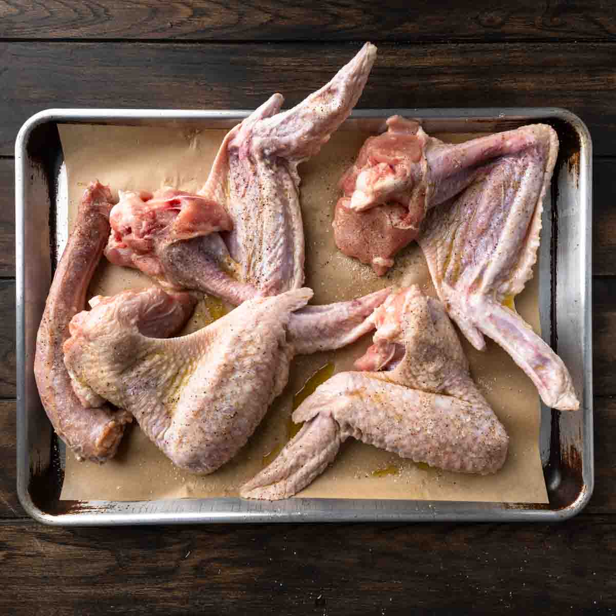 Raw seasoned turkey wings on a baking sheet.
