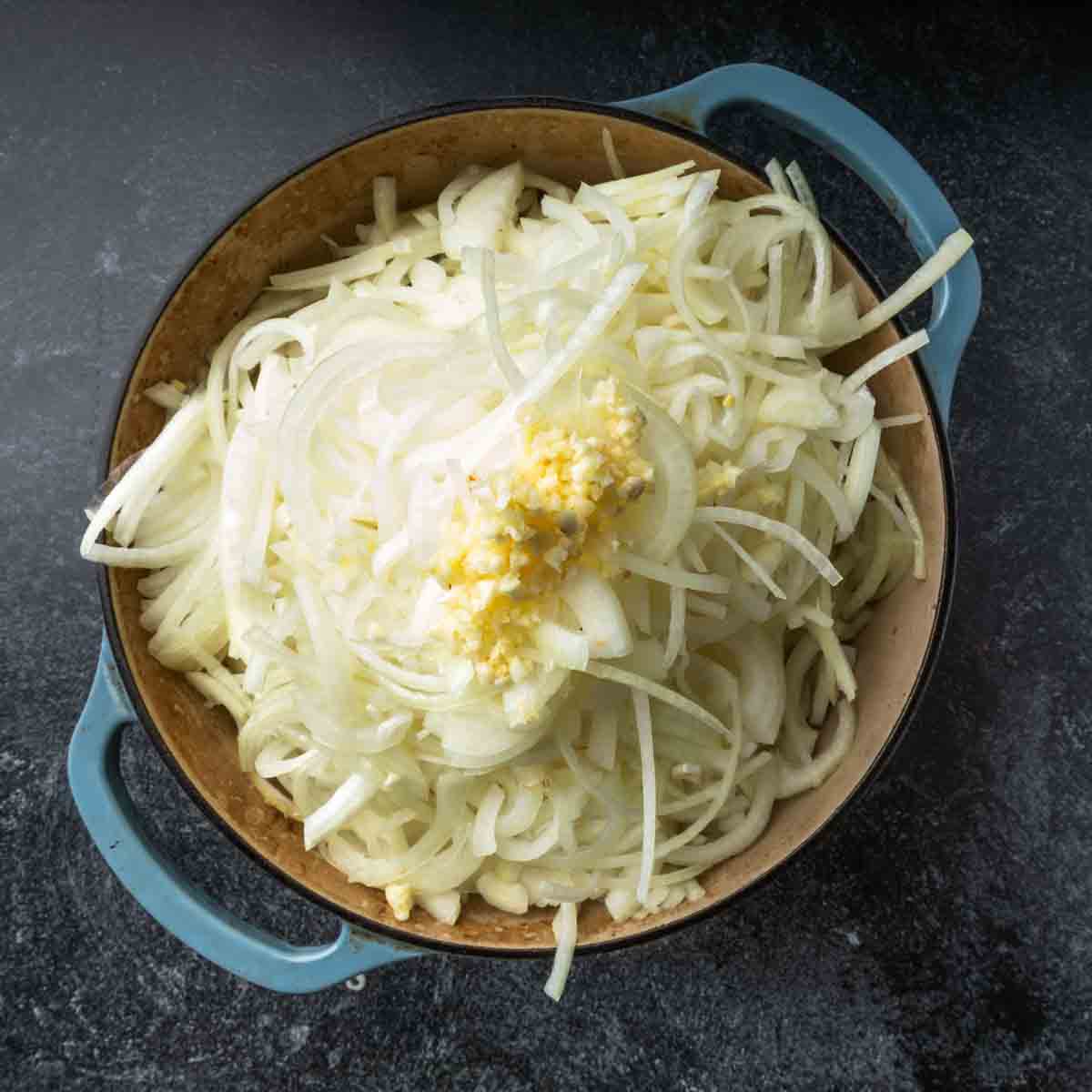 A Dutch oven filled over the brim with sliced onions and minced garlic. 