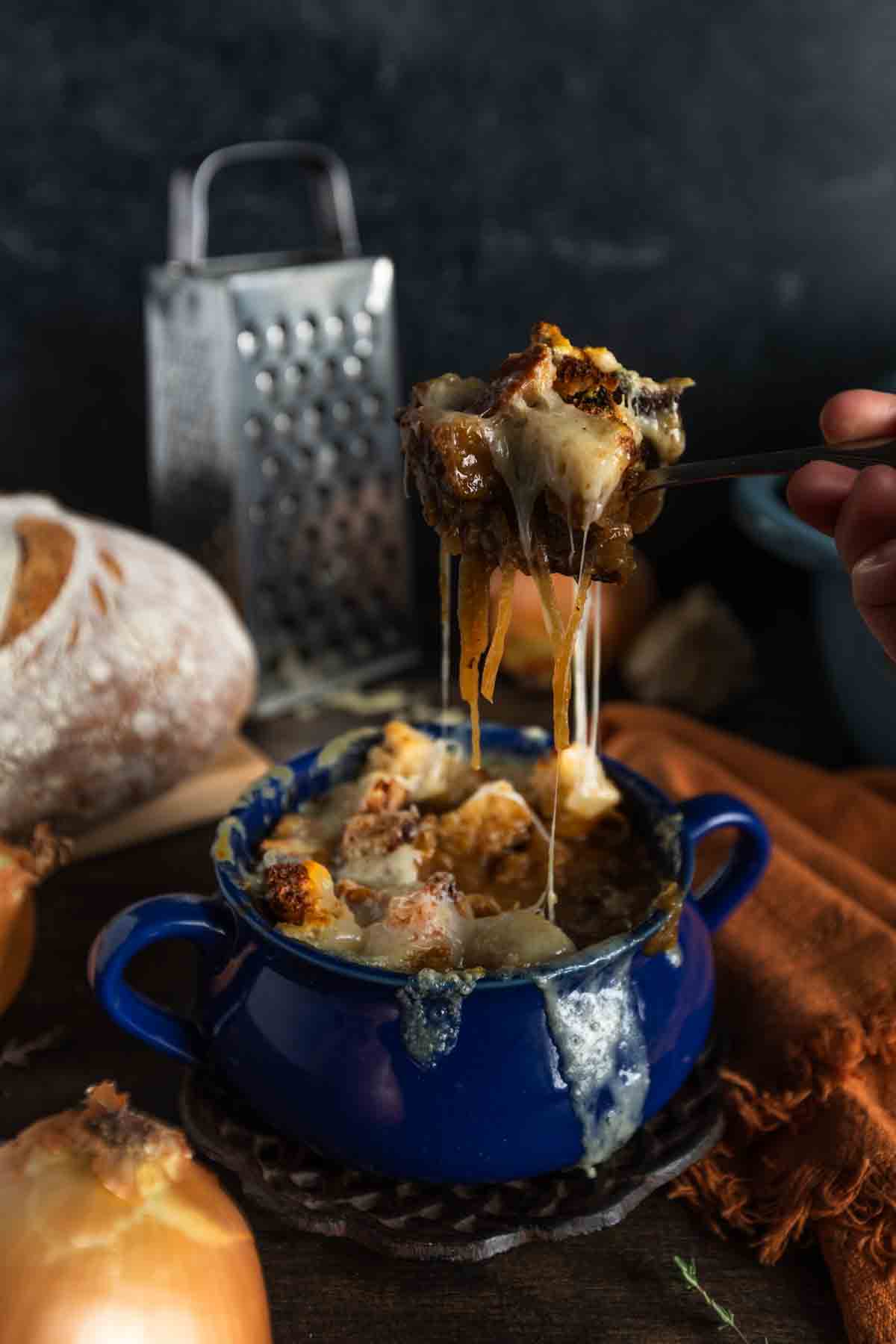 A cheesy pull from a spoonful of French onion beef stew in a crock. 