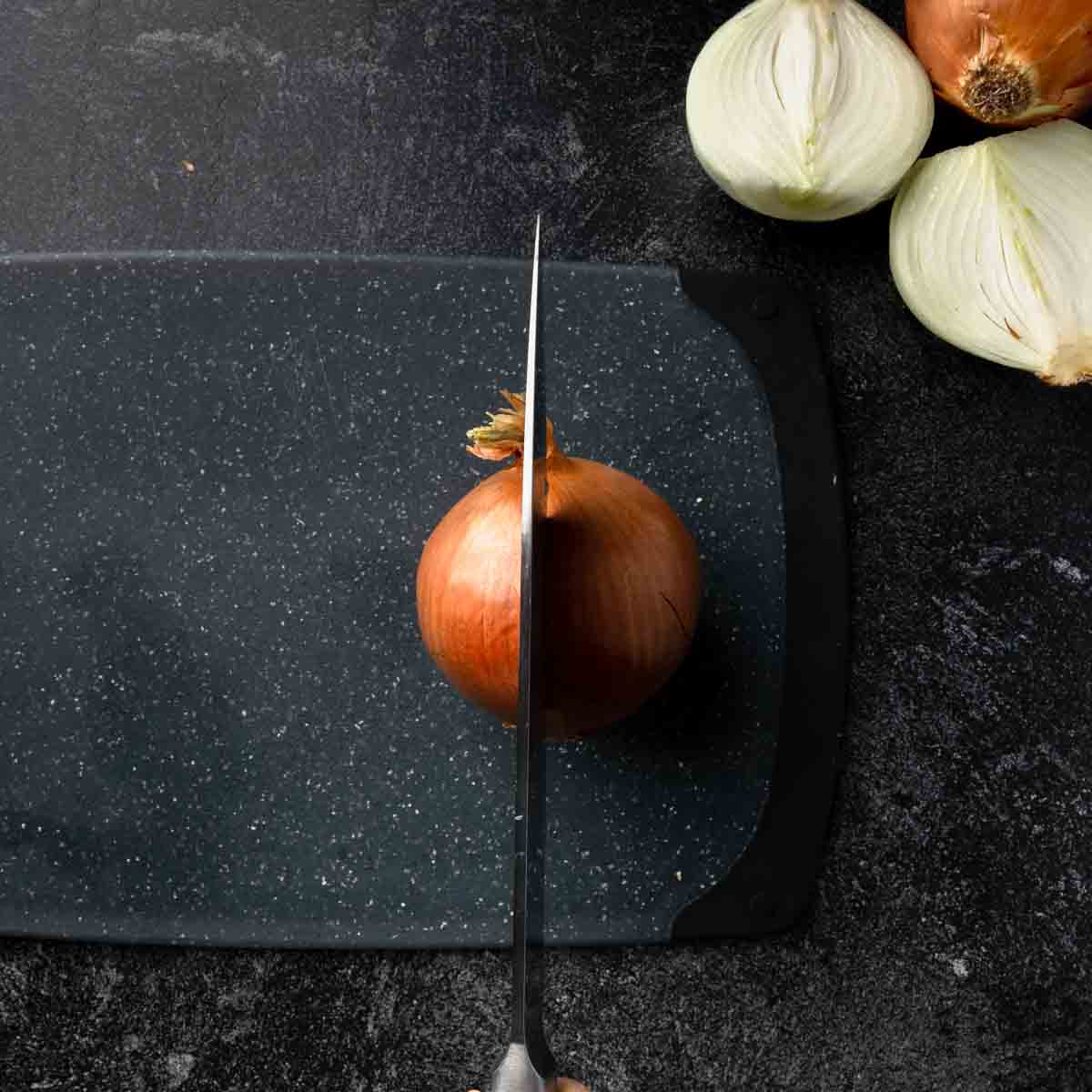 A knife slicing an onion in half, vertically from the root half.