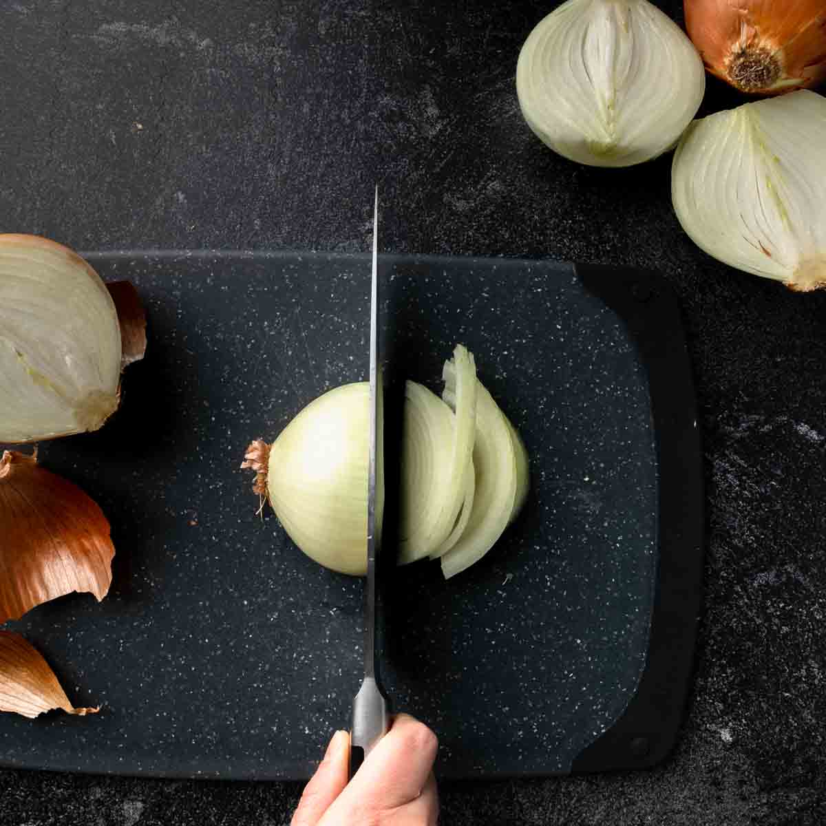 An onion being thinly sliced on a cutting board.