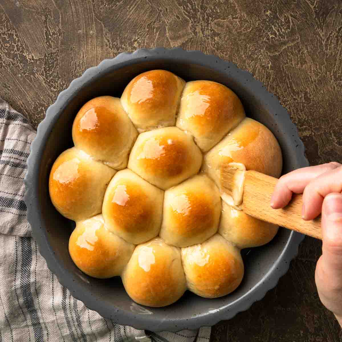 A round plate of fresh baked buns being glazed with maple butter. 