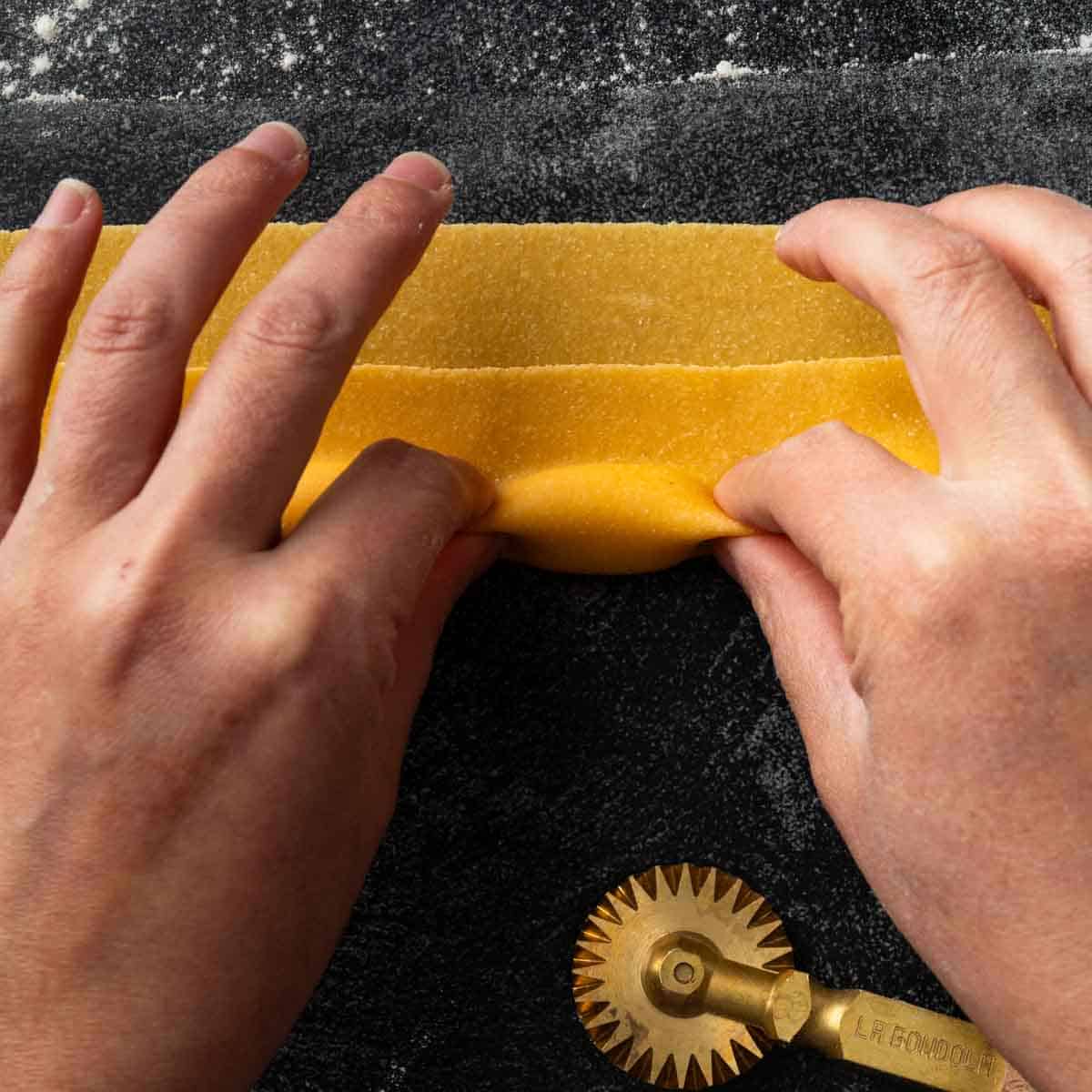 Hands pinching the dough around the farce of a freshly made agnolotti.