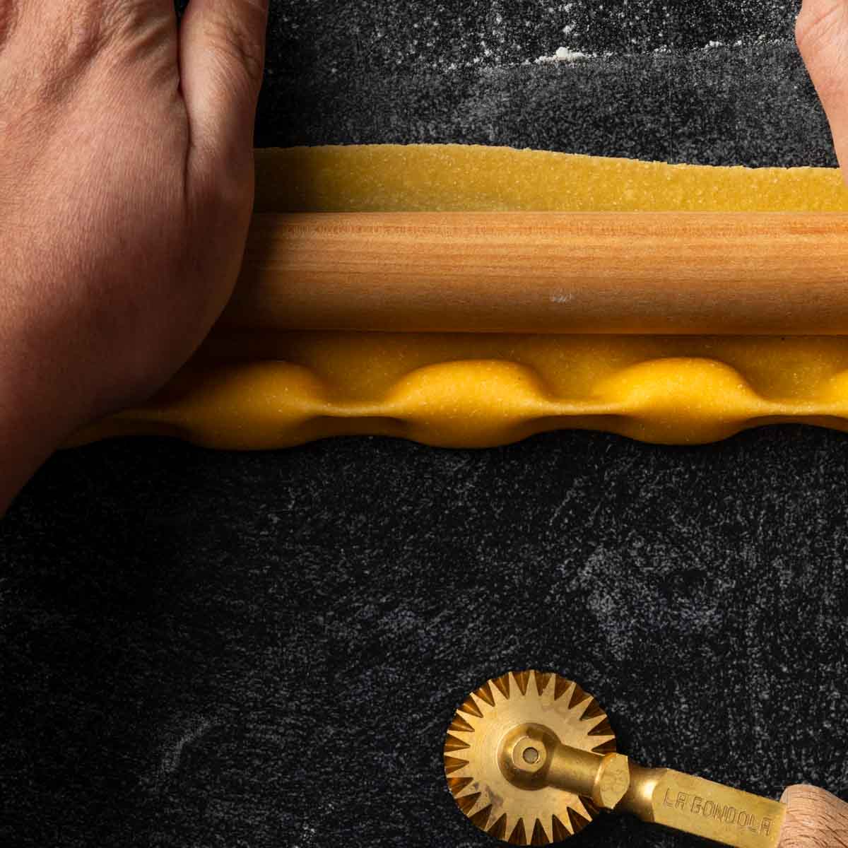 A rolling pin, sealing the upper edge of a strip of agnolotti.