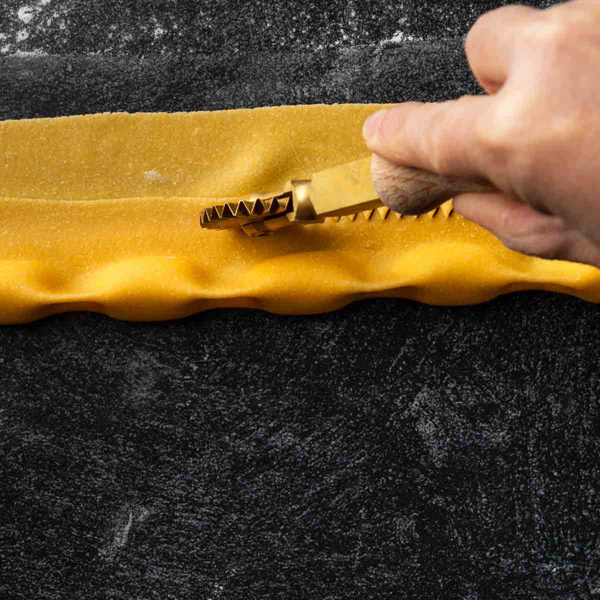 A fluted rotary cutter, cutting away the excess pasta dough above the agnolotti.