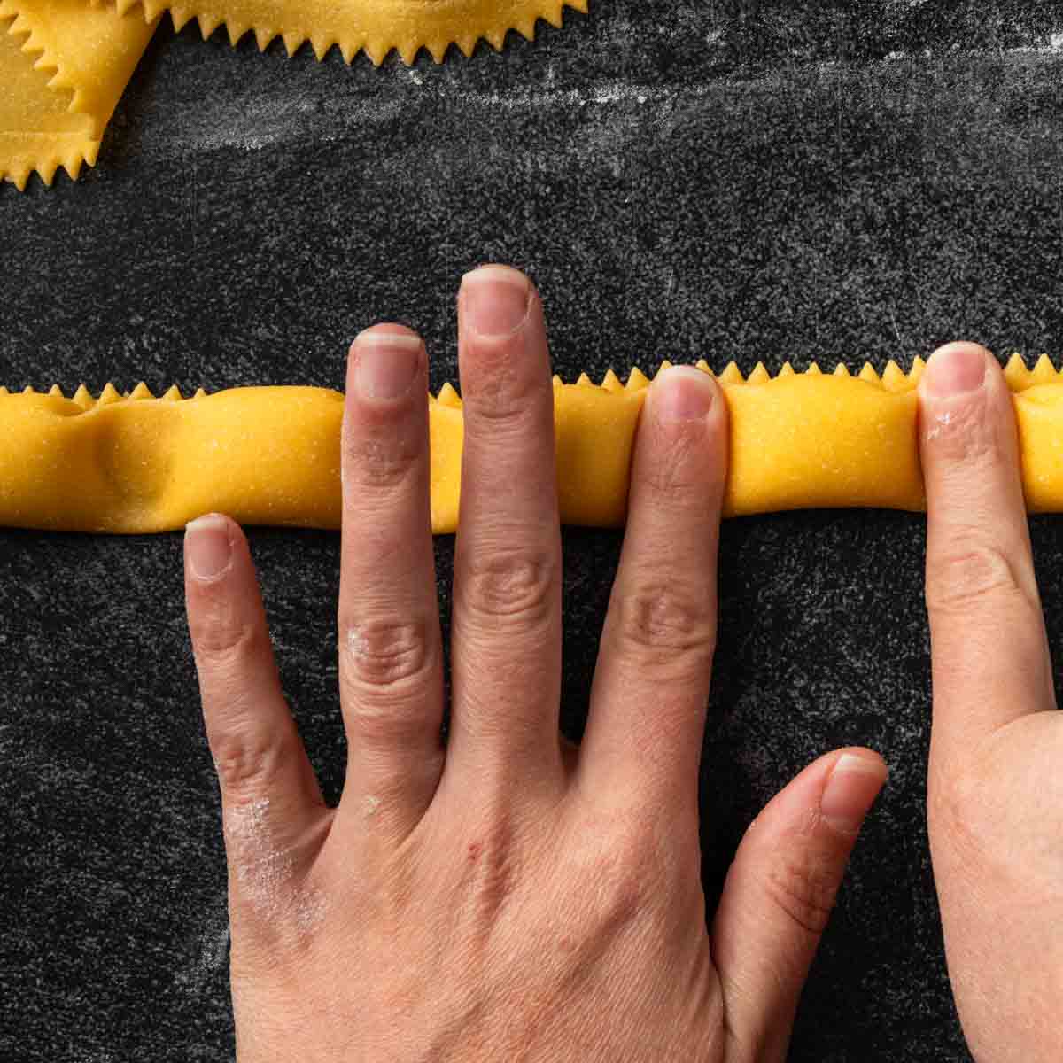 Fingers pinching the dough sealed between a row of agnolotti.