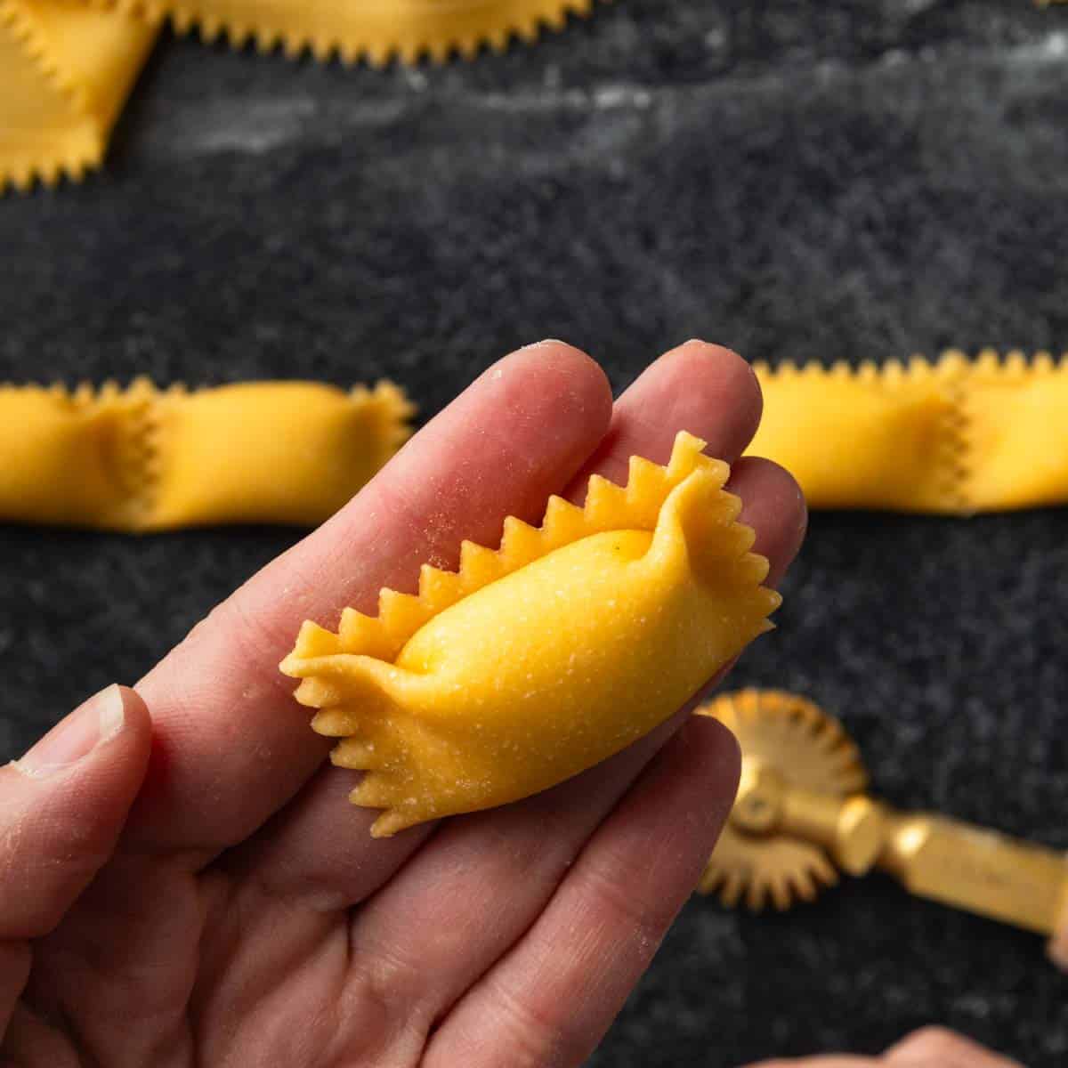 A hand holding up a single agnolotti pasta pocket.