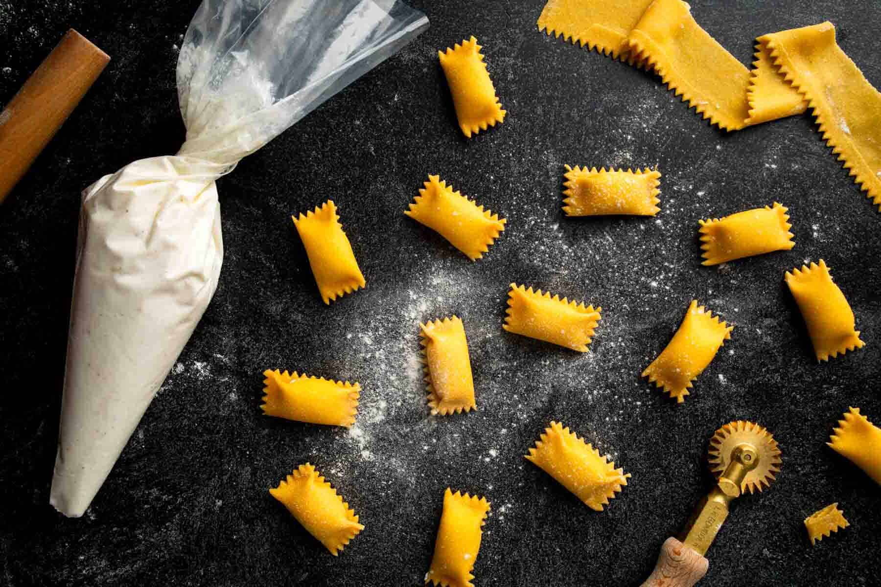 Homemade agnolotti pasta scattered along with a piping bag and brass rotary cutter. 
