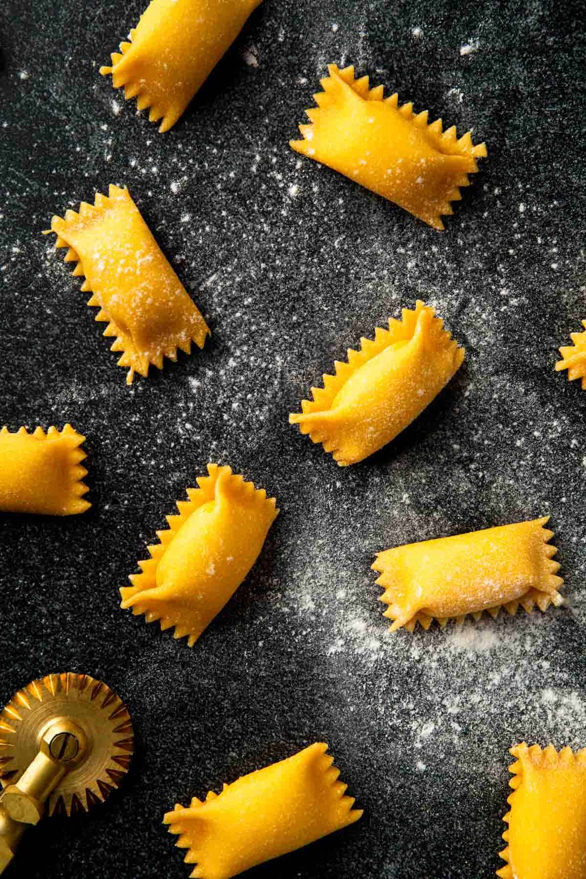 Fresh made agnolotti scattered on a floured countertop.